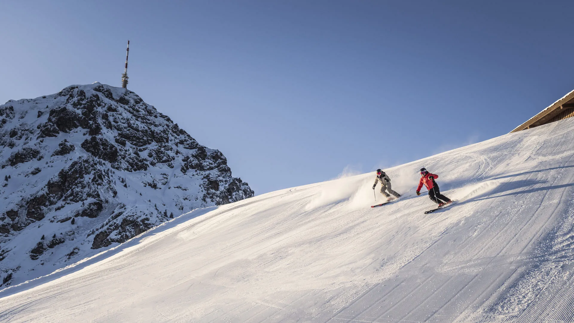 Zwei Skifahrer auf einer sonnigen Piste unterhalb des Gipfels